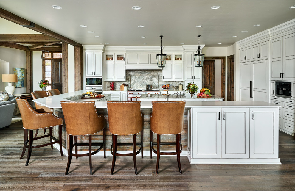 Design ideas for a large country u-shaped kitchen in Portland with white cabinets, quartz benchtops, stone tile splashback, panelled appliances, multiple islands, grey splashback, dark hardwood floors, brown floor, white benchtop and recessed-panel cabinets.