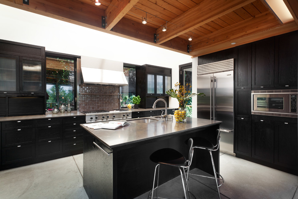 Large contemporary u-shaped eat-in kitchen in San Francisco with an undermount sink, shaker cabinets, dark wood cabinets, limestone benchtops, metallic splashback, glass tile splashback, stainless steel appliances, concrete floors, with island, grey floor and brown benchtop.