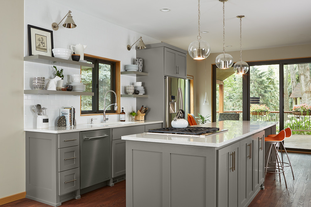 This is an example of a transitional galley kitchen in Minneapolis with shaker cabinets, grey cabinets, white splashback, subway tile splashback, stainless steel appliances, dark hardwood floors and with island.