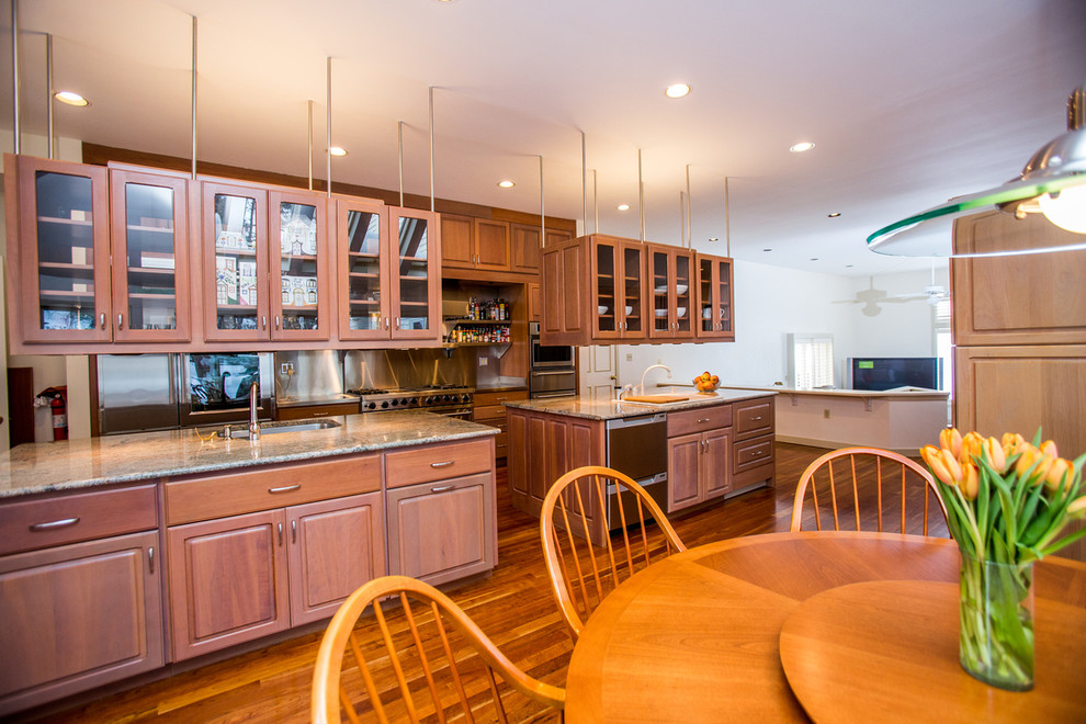 Design ideas for an expansive transitional u-shaped kitchen in Boston with a drop-in sink, recessed-panel cabinets, medium wood cabinets, granite benchtops, stainless steel appliances, medium hardwood floors and multiple islands.