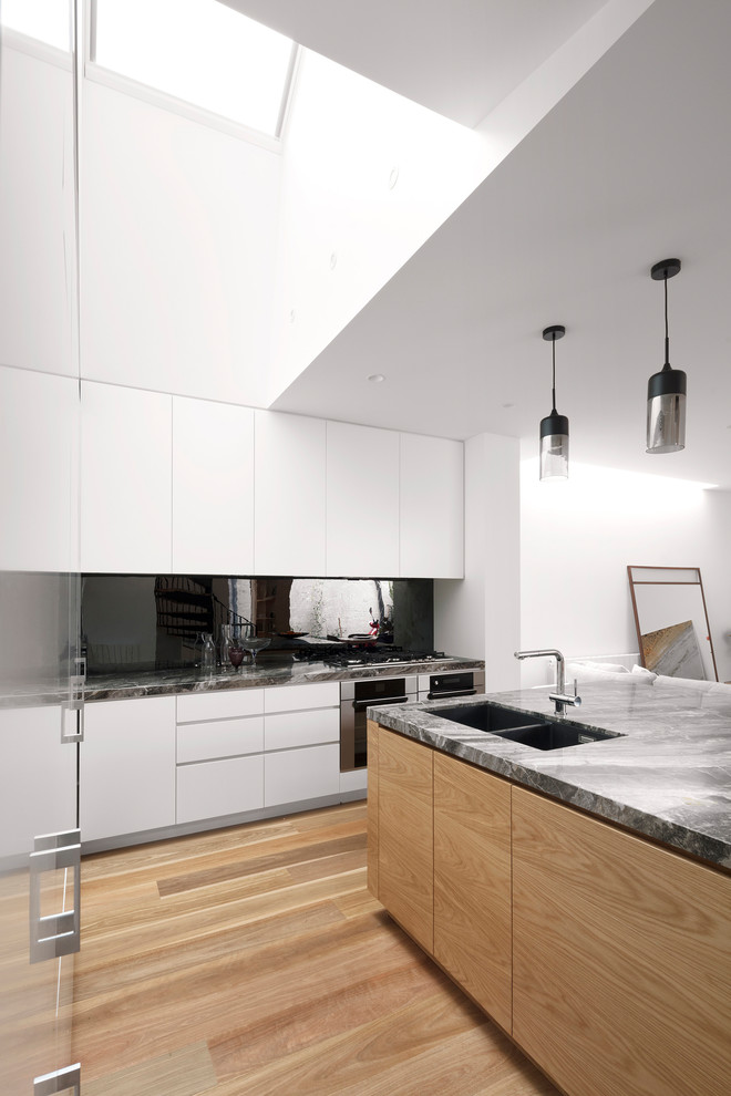Design ideas for a mid-sized contemporary l-shaped open plan kitchen in Melbourne with an undermount sink, flat-panel cabinets, medium wood cabinets, marble benchtops, black splashback, mirror splashback, stainless steel appliances, medium hardwood floors and with island.