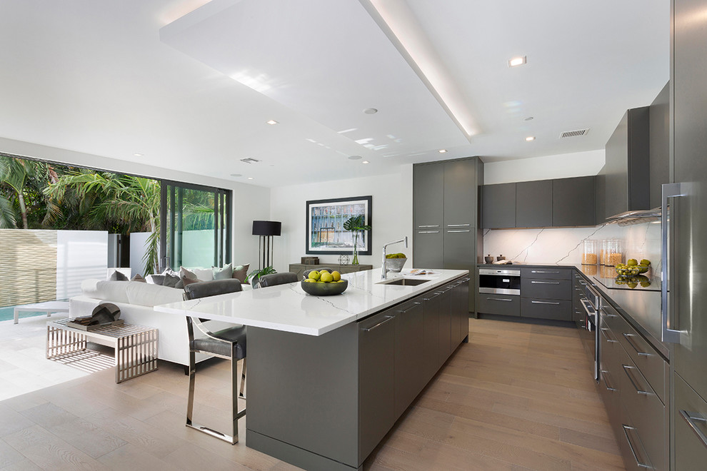 Photo of a large modern l-shaped open plan kitchen in Other with an undermount sink, flat-panel cabinets, grey cabinets, marble benchtops, white splashback, marble splashback, stainless steel appliances, medium hardwood floors, with island, brown floor and white benchtop.