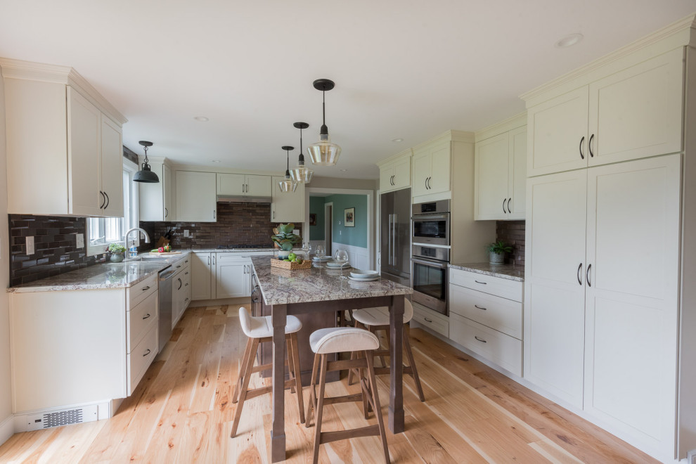 Example of a mid-sized transitional u-shaped light wood floor and brown floor eat-in kitchen design in Boston with an undermount sink, shaker cabinets, white cabinets, granite countertops, brown backsplash, glass tile backsplash, stainless steel appliances, an island and multicolored countertops