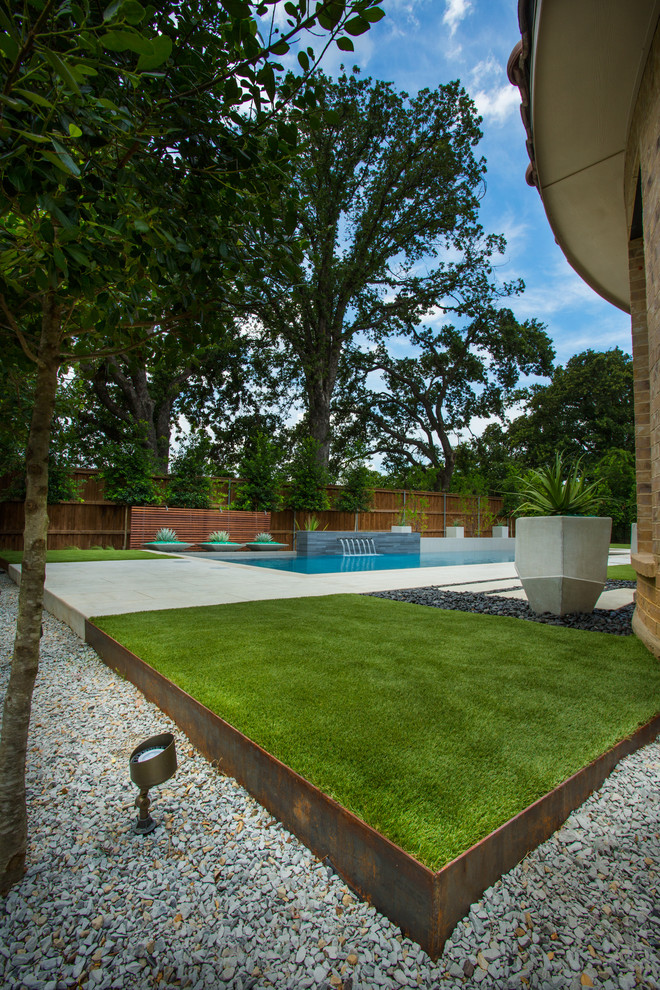 This is an example of a mid-sized modern backyard rectangular pool in Dallas with a water feature and decking.