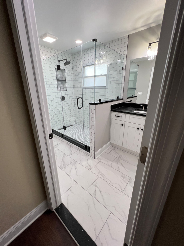 This is an example of a mid-sized modern master bathroom in Other with shaker cabinets, white cabinets, a corner shower, a two-piece toilet, white tile, subway tile, grey walls, an undermount sink, engineered quartz benchtops, white floor, a hinged shower door, black benchtops, a shower seat and a single vanity.