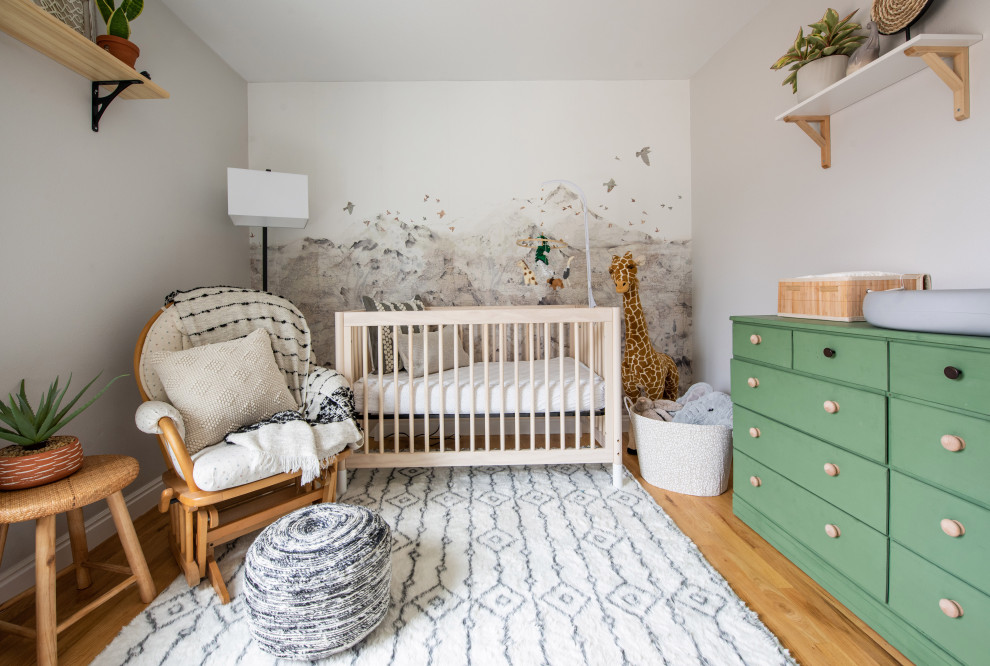 This is an example of a small bohemian gender neutral nursery in Denver with beige walls, light hardwood flooring and wallpapered walls.