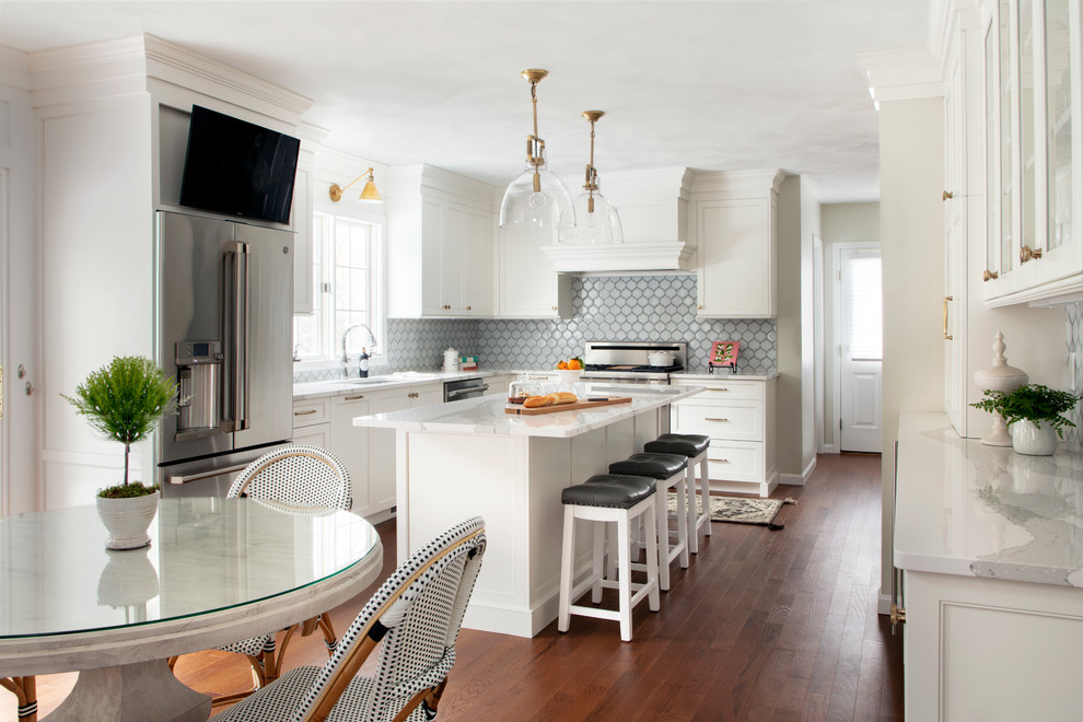 Photo of a transitional u-shaped eat-in kitchen in Boston with white cabinets, quartz benchtops, blue splashback, porcelain splashback, stainless steel appliances, medium hardwood floors, with island, brown floor, grey benchtop, an undermount sink and shaker cabinets.