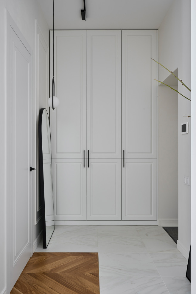 На фото: коридор среднего размера: освещение в стиле неоклассика (современная классика) с белыми стенами, полом из керамогранита и белым полом с