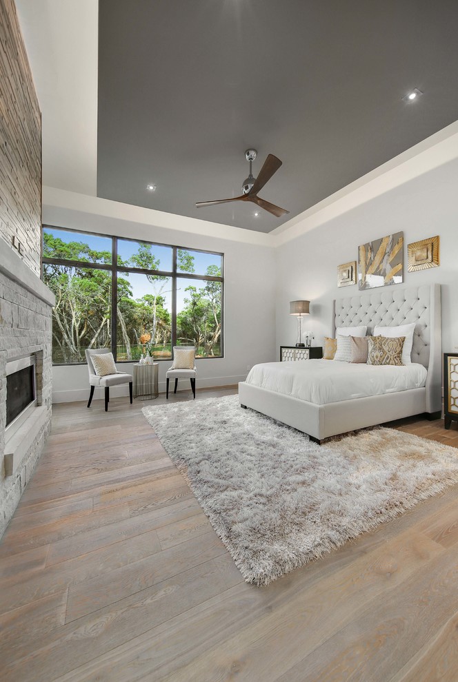 Expansive contemporary master bedroom in Austin with grey walls, light hardwood floors, a standard fireplace, a stone fireplace surround and grey floor.