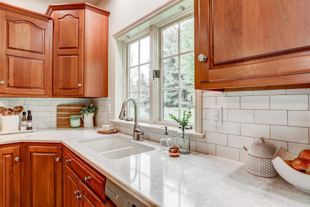 Foto på ett mellanstort vintage vit kök, med en dubbel diskho, luckor med upphöjd panel, skåp i mellenmörkt trä, bänkskiva i kvarts, vitt stänkskydd, stänkskydd i tunnelbanekakel, rostfria vitvaror och en köksö