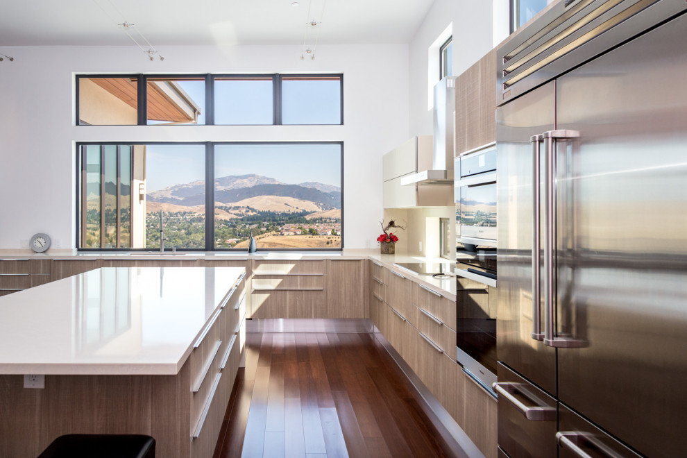 This is an example of a large modern u-shaped open plan kitchen in San Francisco with an undermount sink, flat-panel cabinets, beige cabinets, quartz benchtops, white splashback, stainless steel appliances, with island and white benchtop.