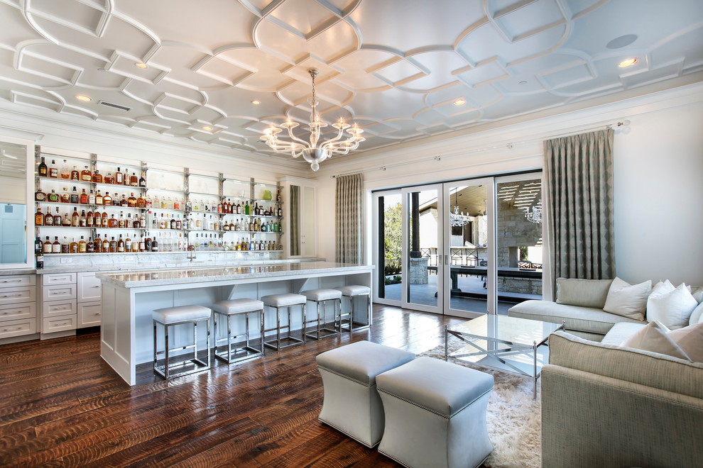 Inspiration for a large transitional seated home bar in Dallas with recessed-panel cabinets, white cabinets, marble benchtops, white splashback, stone tile splashback, medium hardwood floors, brown floor and white benchtop.
