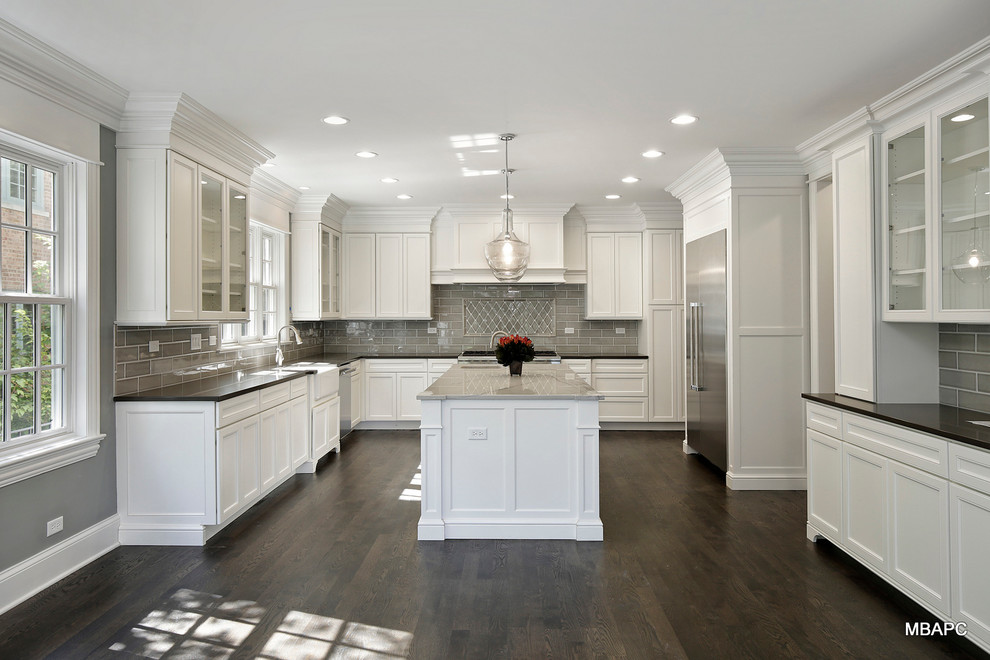 This is an example of a large traditional u-shaped eat-in kitchen in Chicago with a farmhouse sink, flat-panel cabinets, white cabinets, quartzite benchtops, grey splashback, ceramic splashback, stainless steel appliances, dark hardwood floors and with island.