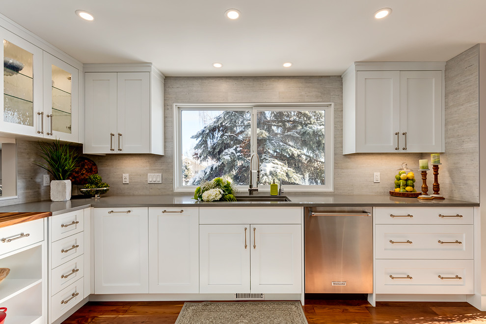 Mid-sized transitional l-shaped medium tone wood floor enclosed kitchen photo in Calgary with an undermount sink, recessed-panel cabinets, white cabinets, quartz countertops, gray backsplash, porcelain backsplash, stainless steel appliances and an island