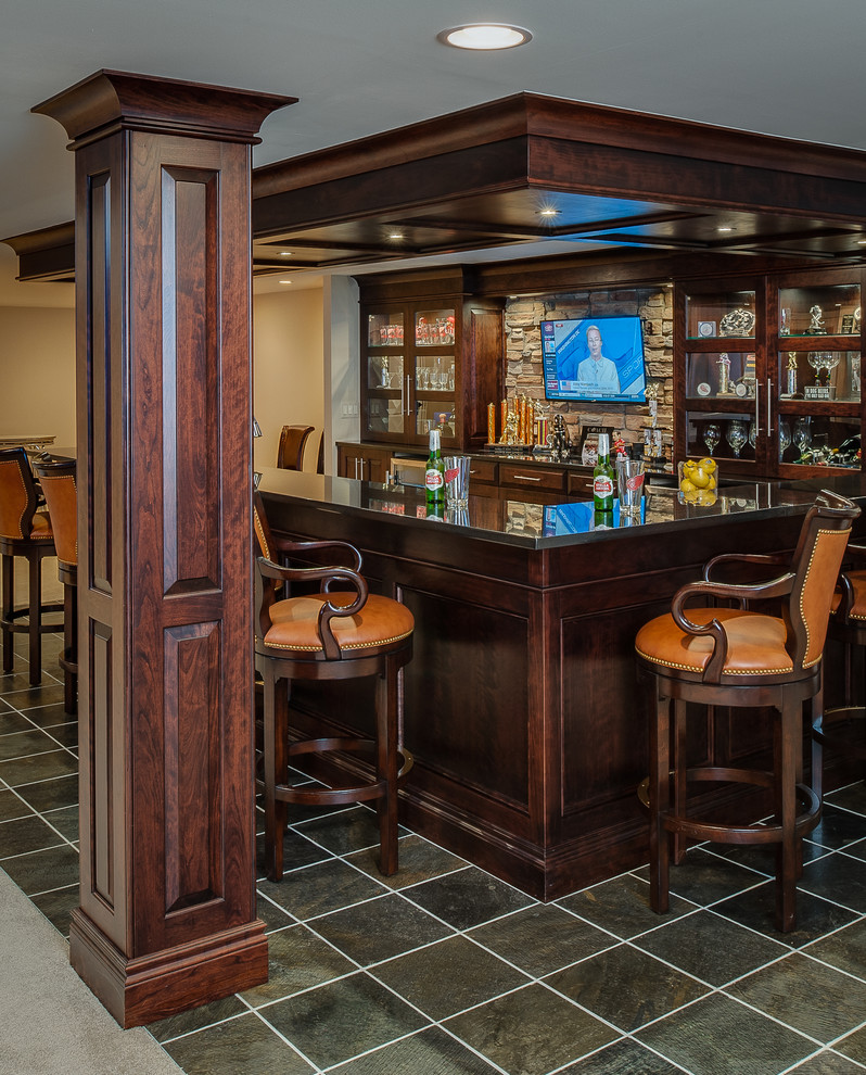 Large transitional galley seated home bar in Detroit with an undermount sink, dark wood cabinets, granite benchtops, beige splashback, stone tile splashback, slate floors and recessed-panel cabinets.