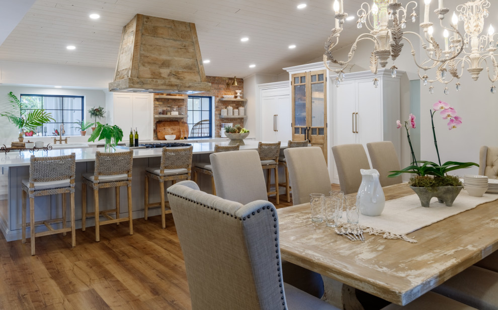 Idée de décoration pour une très grande salle à manger ouverte sur le salon champêtre avec un mur blanc, un sol en vinyl, une cheminée double-face, un manteau de cheminée en pierre de parement, un sol marron et un plafond en bois.