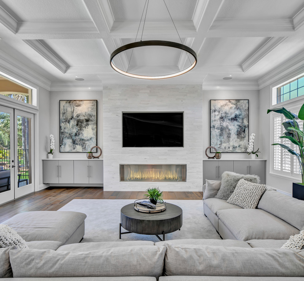 Großes, Abgetrenntes Modernes Wohnzimmer mit weißer Wandfarbe, braunem Holzboden, Kamin, Kaminumrandung aus gestapelten Steinen, Multimediawand, braunem Boden und Kassettendecke in Tampa