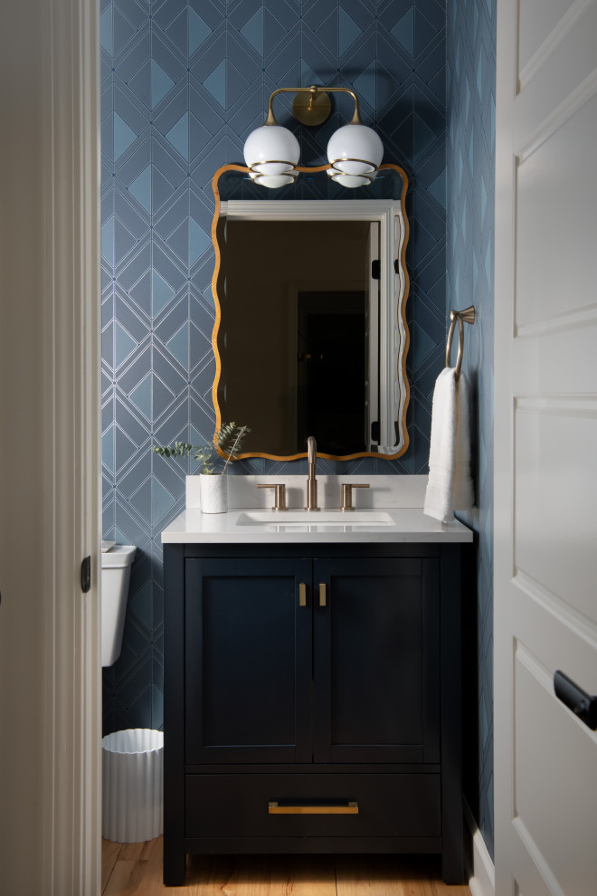 Powder room - transitional medium tone wood floor, brown floor and wallpaper powder room idea in Charlotte with shaker cabinets, black cabinets, blue walls, an undermount sink, gray countertops and a freestanding vanity