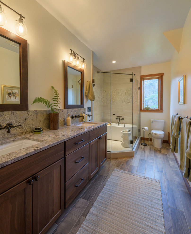 Photo of a mid-sized contemporary master wet room bathroom with shaker cabinets, medium wood cabinets, a freestanding tub, a one-piece toilet, beige tile, pebble tile, beige walls, dark hardwood floors, an undermount sink, granite benchtops, grey floor and a hinged shower door.