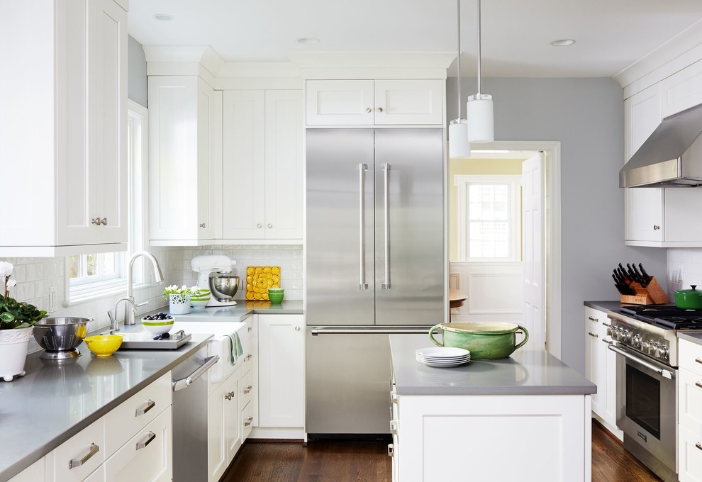 Mid-sized transitional u-shaped separate kitchen in DC Metro with shaker cabinets, white cabinets, white splashback, dark hardwood floors, with island, brown floor, a farmhouse sink, solid surface benchtops, subway tile splashback and stainless steel appliances.