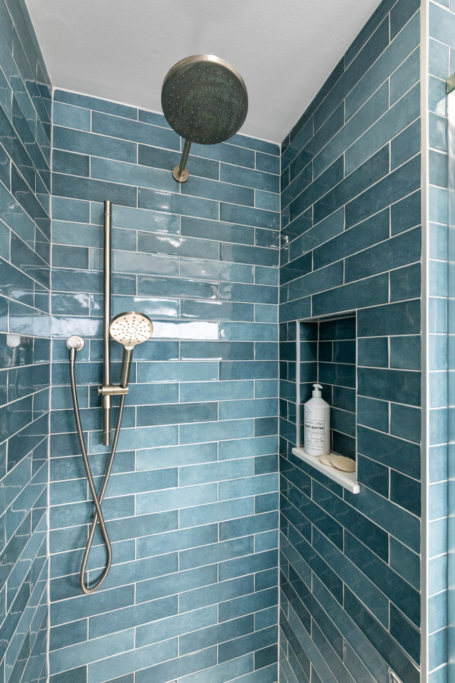 This is an example of a large beach style ensuite bathroom in Ottawa with a built-in shower, blue tiles, blue walls, a wall niche, shaker cabinets, light wood cabinets, a freestanding bath, a two-piece toilet, ceramic tiles, ceramic flooring, a submerged sink, engineered stone worktops, blue floors, a hinged door, white worktops, double sinks and a freestanding vanity unit.