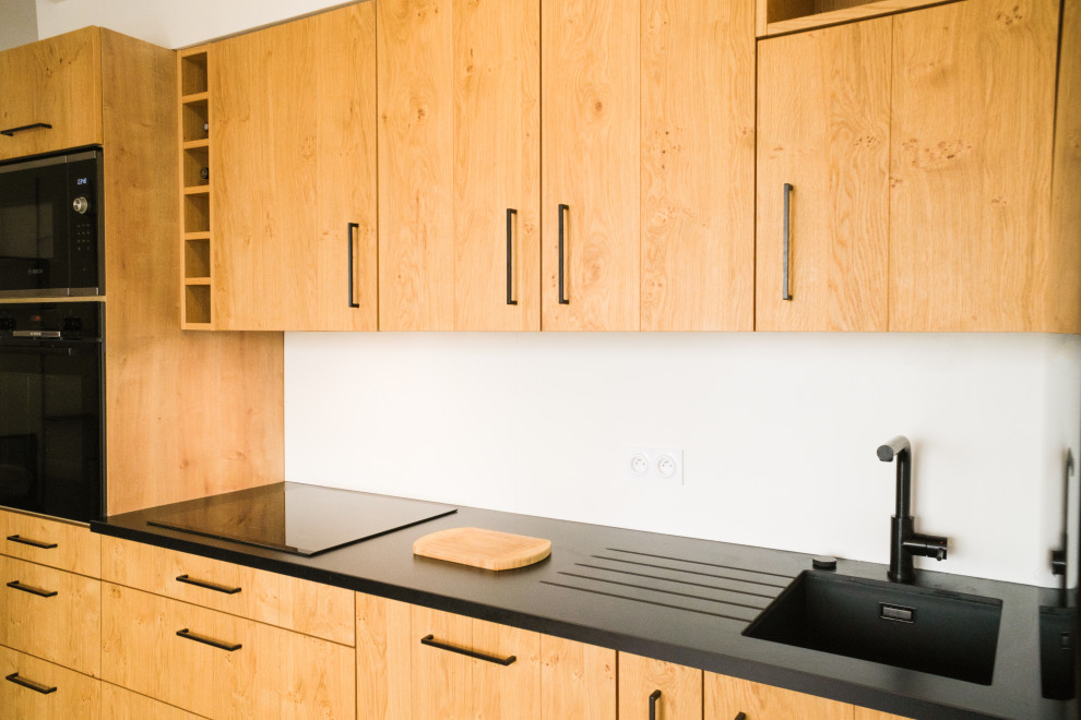 Immagine di una cucina minimalista di medie dimensioni con ante in legno chiaro, elettrodomestici neri, nessuna isola, top nero e lavello integrato