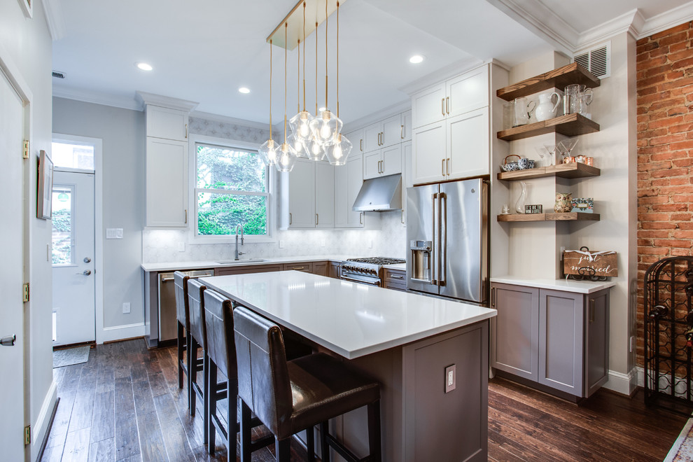 Example of a large transitional l-shaped medium tone wood floor and brown floor eat-in kitchen design in DC Metro with an island, an undermount sink, shaker cabinets, white cabinets, solid surface countertops, white backsplash, ceramic backsplash, stainless steel appliances and white countertops