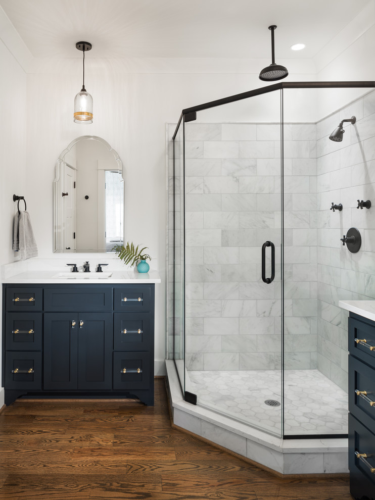 Inspiration for a mid-sized arts and crafts master bathroom in Birmingham with recessed-panel cabinets, blue cabinets, a corner shower, a two-piece toilet, white tile, ceramic tile, white walls, medium hardwood floors, an undermount sink, marble benchtops, brown floor and a hinged shower door.