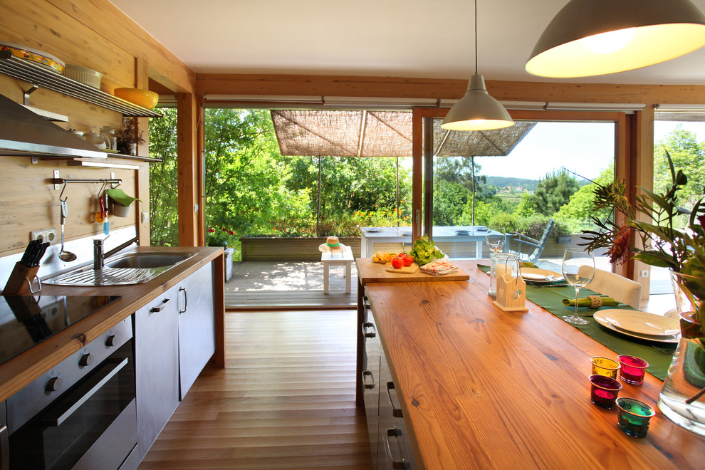 This is an example of a mid-sized tropical single-wall eat-in kitchen in Other with a drop-in sink, flat-panel cabinets, stainless steel cabinets, wood benchtops, metallic splashback, metal splashback, stainless steel appliances, medium hardwood floors, with island and multi-coloured floor.