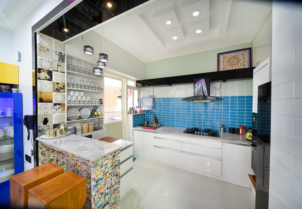 Inspiration for a contemporary l-shaped kitchen/diner in Bengaluru with flat-panel cabinets, white cabinets, blue splashback, mosaic tiled splashback, black appliances, a breakfast bar, white floors and grey worktops.