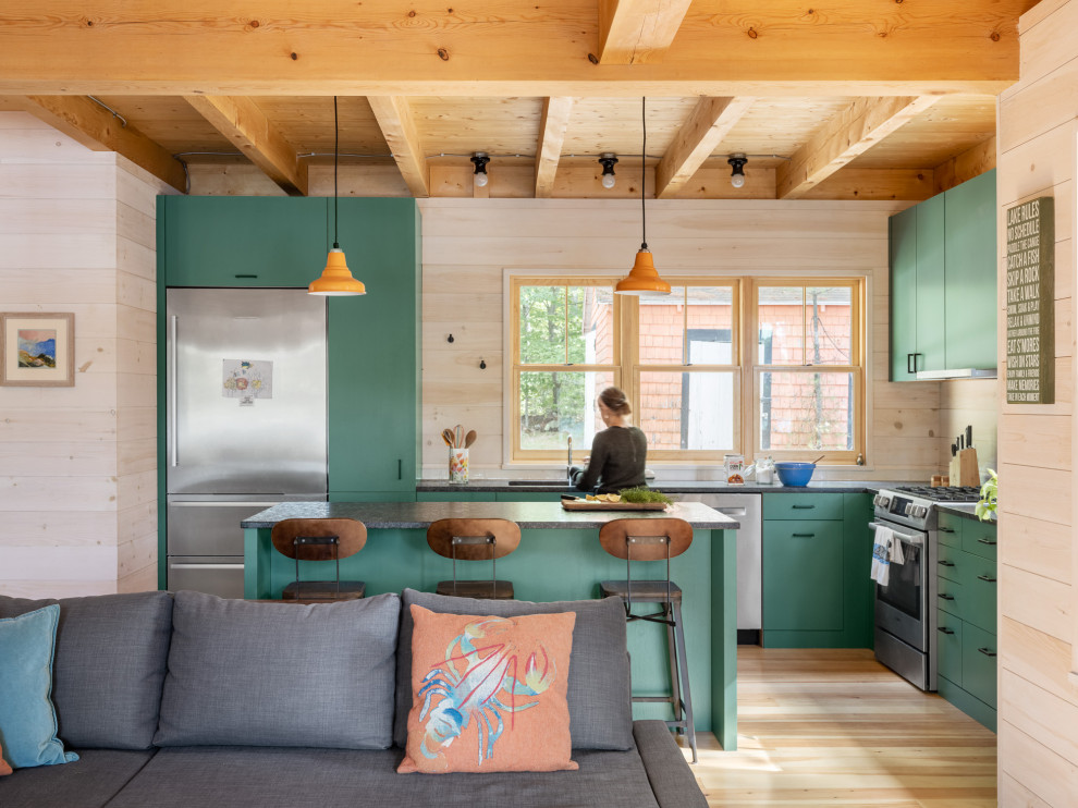 Country l-shaped kitchen in Portland Maine with an undermount sink, flat-panel cabinets, green cabinets, stainless steel appliances, light hardwood floors, with island, beige floor, black benchtop and exposed beam.