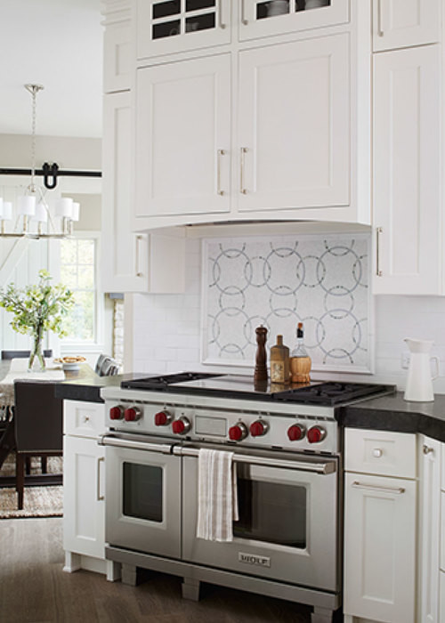Mid-sized transitional galley separate kitchen in Chicago with white cabinets, stainless steel appliances, with island, a farmhouse sink, shaker cabinets, marble benchtops, white splashback, glass tile splashback and medium hardwood floors.