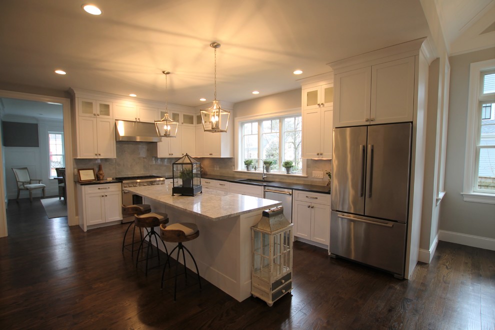 This is an example of a large transitional l-shaped eat-in kitchen in Boston with an undermount sink, shaker cabinets, white cabinets, granite benchtops, beige splashback, marble splashback, stainless steel appliances, dark hardwood floors, with island and brown floor.
