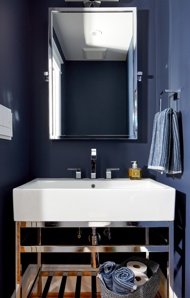 This is an example of a small transitional powder room in DC Metro with furniture-like cabinets, blue walls, light hardwood floors and a console sink.