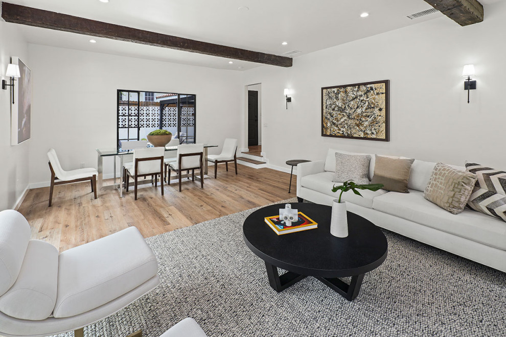 Example of a large transitional open concept medium tone wood floor, brown floor and exposed beam living room design in Los Angeles with white walls, a standard fireplace, a concrete fireplace and no tv