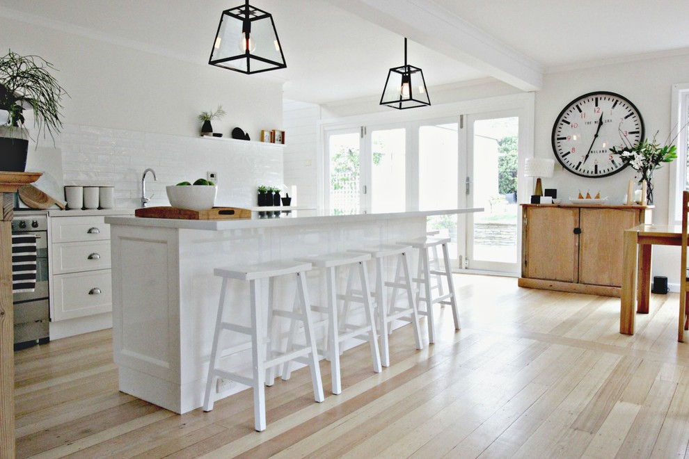 Transitional galley open plan kitchen in Hobart with an undermount sink, white cabinets, quartz benchtops, white splashback, ceramic splashback, stainless steel appliances, medium hardwood floors and with island.