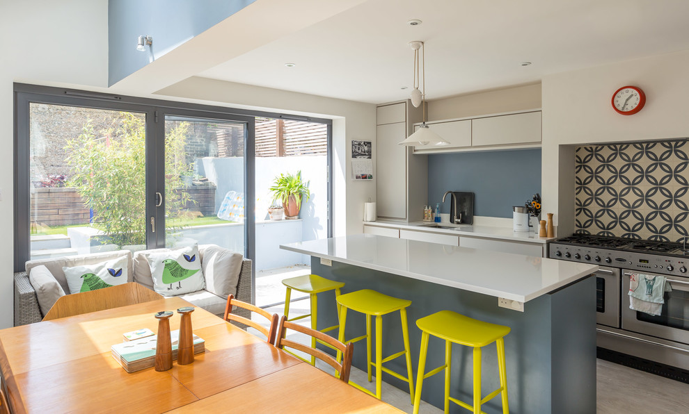 This is an example of a contemporary galley eat-in kitchen in Sussex with flat-panel cabinets, white cabinets, multi-coloured splashback, stainless steel appliances and with island.