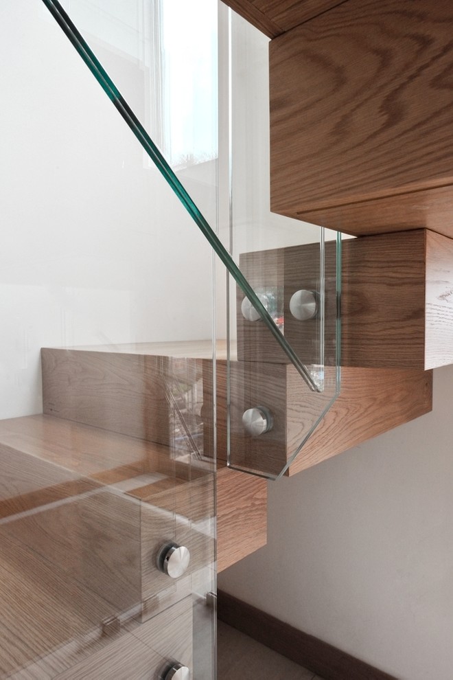 Immagine di una grande scala curva minimal con pedata in legno, alzata in vetro e parapetto in vetro
