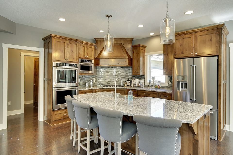 Example of a transitional l-shaped medium tone wood floor eat-in kitchen design in Minneapolis with an undermount sink, shaker cabinets, medium tone wood cabinets, granite countertops, stainless steel appliances and an island
