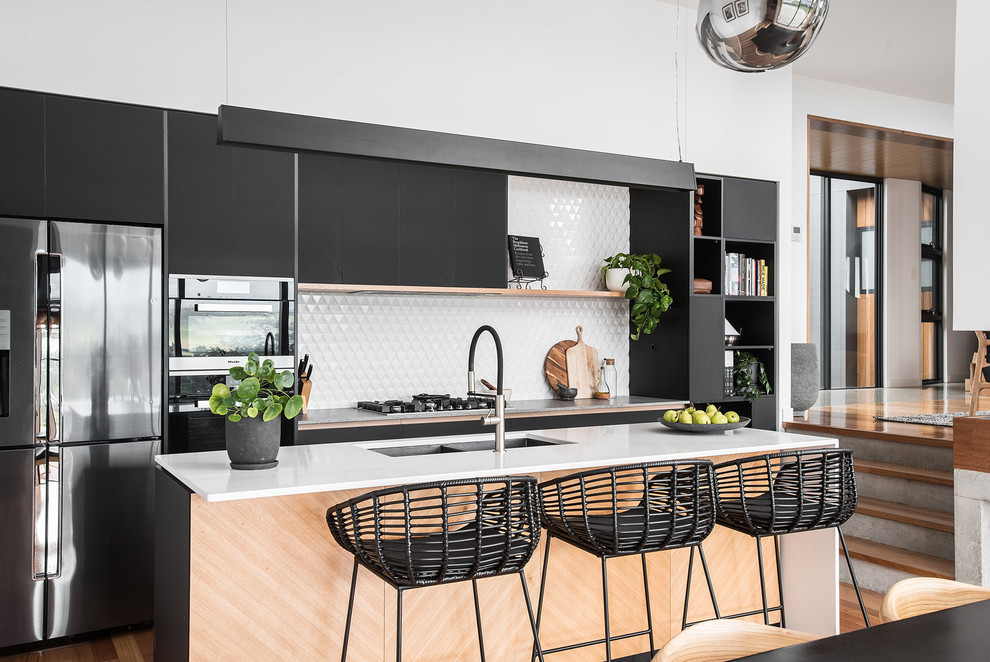 Photo of a contemporary kitchen in Hobart with a double-bowl sink, flat-panel cabinets, black cabinets, white splashback, stainless steel appliances, medium hardwood floors, with island, brown floor and white benchtop.