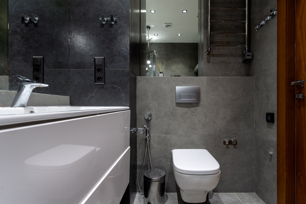 Пример оригинального дизайна: маленькая серо-белая ванная комната в стиле фьюжн с плоскими фасадами, белыми фасадами, ванной в нише, душем над ванной, инсталляцией, черной плиткой, керамогранитной плиткой, серыми стенами, полом из керамогранита, душевой кабиной, подвесной раковиной, столешницей из кварцита, серым полом, душем с раздвижными дверями, белой столешницей, гигиеническим душем, тумбой под одну раковину и подвесной тумбой для на участке и в саду