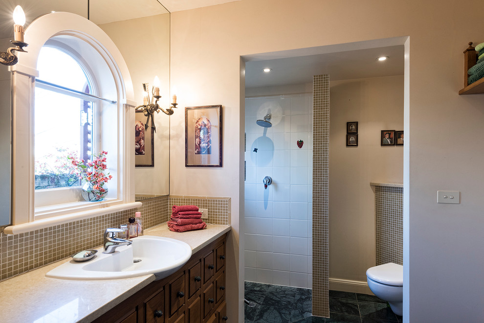 This is an example of a large mediterranean master bathroom in Adelaide with furniture-like cabinets, medium wood cabinets, a wall-mount toilet, beige tile, mosaic tile, beige walls, marble floors, an integrated sink and marble benchtops.
