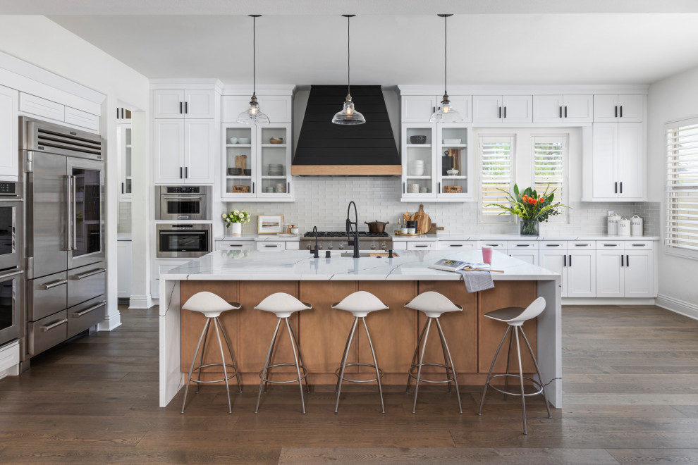 Design ideas for a small transitional l-shaped open plan kitchen in Orange County with shaker cabinets, white cabinets, quartzite benchtops, white splashback, glass tile splashback, stainless steel appliances, dark hardwood floors, with island, brown floor, white benchtop and an undermount sink.