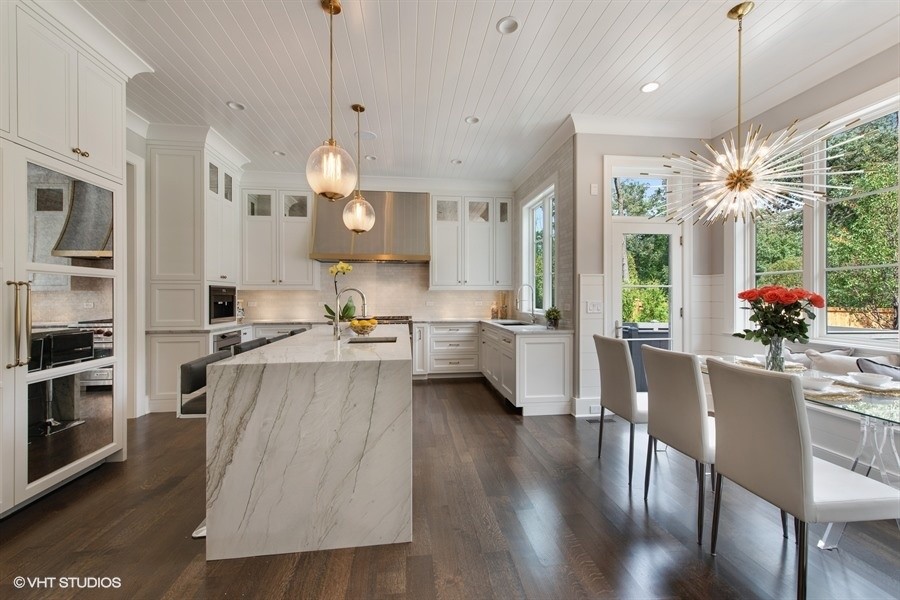 Example of a large transitional u-shaped medium tone wood floor and brown floor eat-in kitchen design in Chicago with a drop-in sink, recessed-panel cabinets, white cabinets, quartzite countertops, gray backsplash, porcelain backsplash, paneled appliances, an island and gray countertops