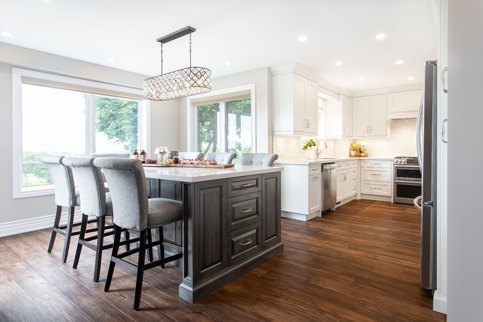 Large transitional u-shaped dark wood floor and brown floor eat-in kitchen photo in Toronto with an undermount sink, recessed-panel cabinets, white cabinets, quartz countertops, white backsplash, ceramic backsplash, stainless steel appliances, an island and white countertops