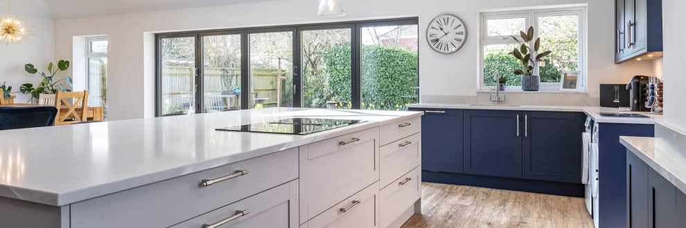 This is an example of a large contemporary open plan kitchen in Oxfordshire with shaker cabinets, blue cabinets, quartzite benchtops, white splashback, light hardwood floors, with island, brown floor and white benchtop.