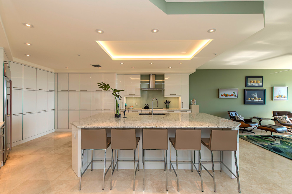 Photo of a contemporary open plan kitchen in New York with an undermount sink, flat-panel cabinets, white cabinets, green splashback, glass sheet splashback, stainless steel appliances, with island, beige floor, multi-coloured benchtop and granite benchtops.