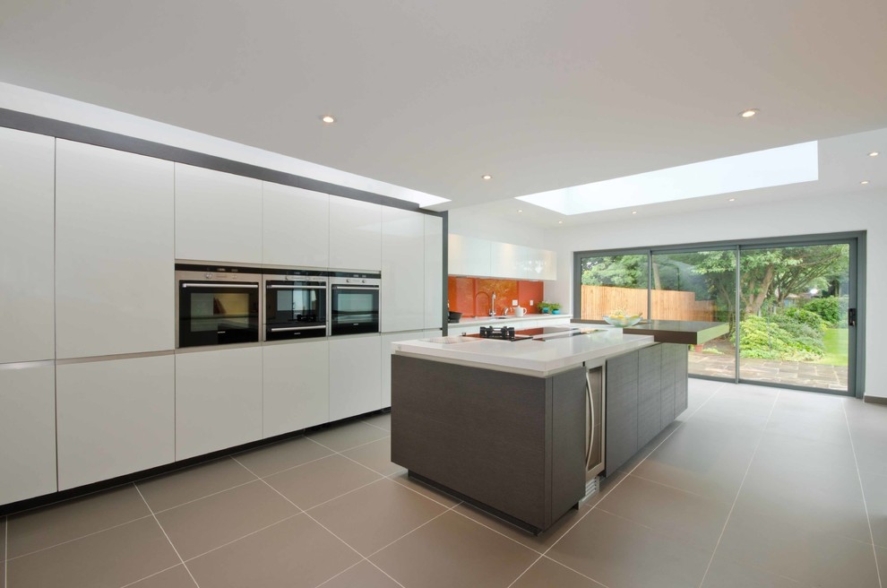 This is an example of a contemporary single-wall separate kitchen in West Midlands with flat-panel cabinets, orange splashback, glass sheet splashback, ceramic floors, with island, an integrated sink and white appliances.
