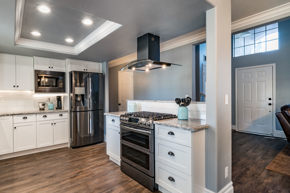 Inspiration for a mid-sized transitional u-shaped dark wood floor and brown floor eat-in kitchen remodel with an undermount sink, shaker cabinets, white cabinets, granite countertops, white backsplash, subway tile backsplash, stainless steel appliances and an island