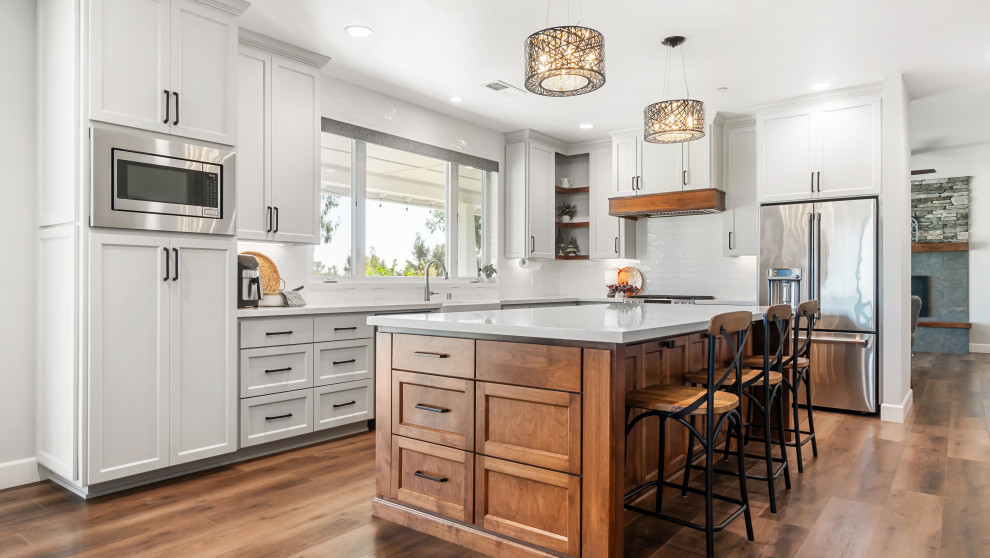 Transitional l-shaped kitchen photo with shaker cabinets, gray cabinets, white backsplash, stainless steel appliances, an island and white countertops